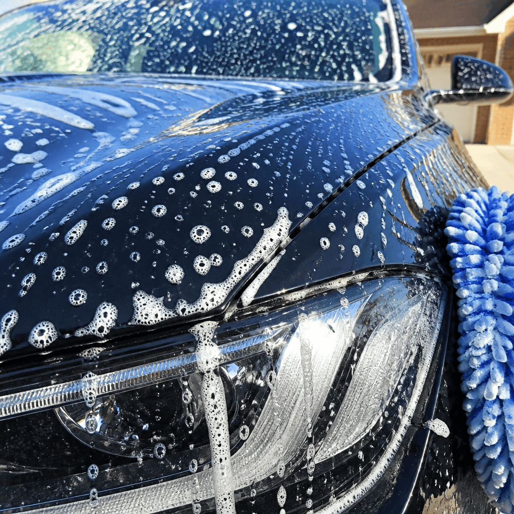 Glossy dark car exterior covered in white foam wash bubbles